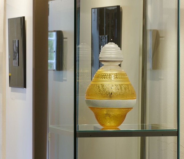 Blick in die Ausstellung. Im Vordergrund eine Vitrine mit einem gelben Glasgefäß mit unterschiedlichen Gravuren von Gérald Vatrin.