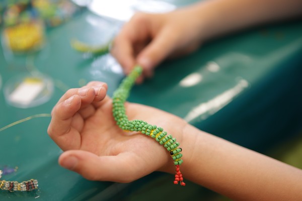 Kinderhand mit einem raupenartigen Tier aus grünen Perlen.
