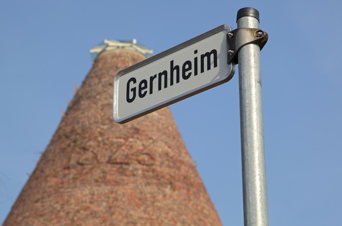 Ein Straßenschild mit der Aufschrift "Gernheim" steht vor dem Glasturm der Glashütte Gernheim.