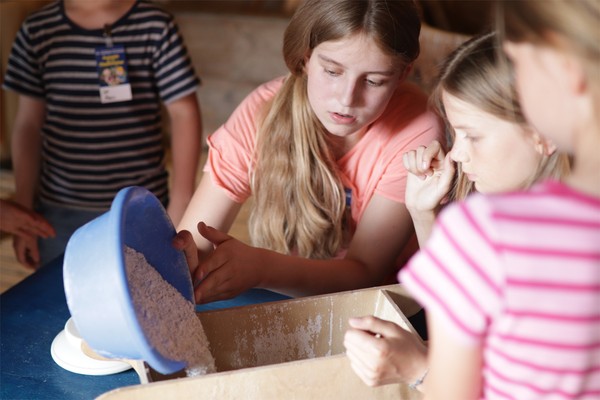 Kinder mischen die für die Glasherstellung nötigen Rohstoffe zusammen.