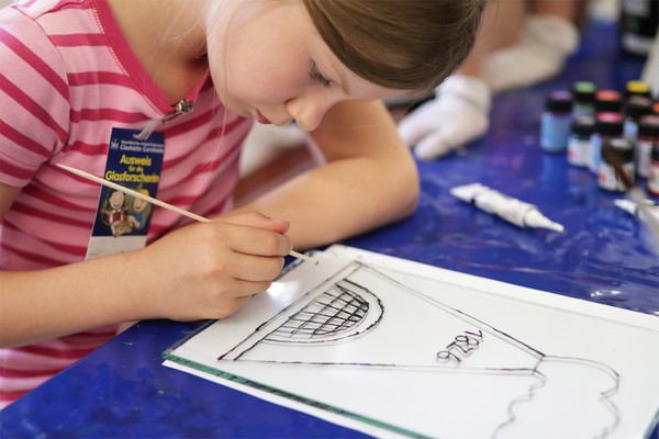 Ein Mädchen malt einen Glasturm auf eine Glasplatte.