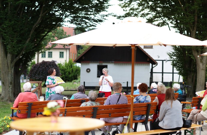Senior:innen sitzen vor zwei Führungskräften, die ein Programm präsentieren