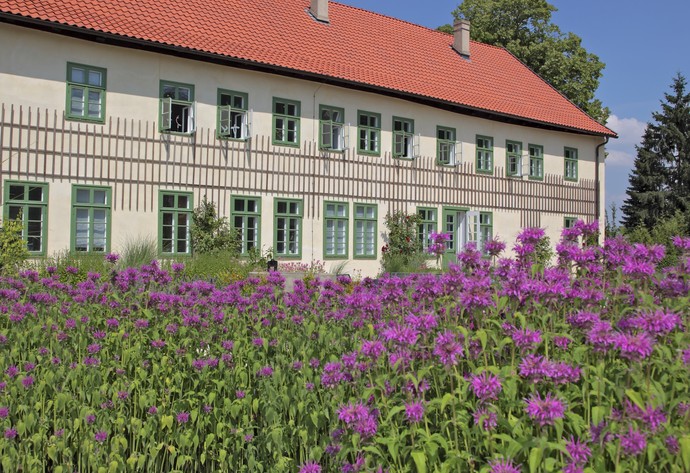 Außenansicht des Herrenhauses mit lila farbenen Blumen im Vordergrund.