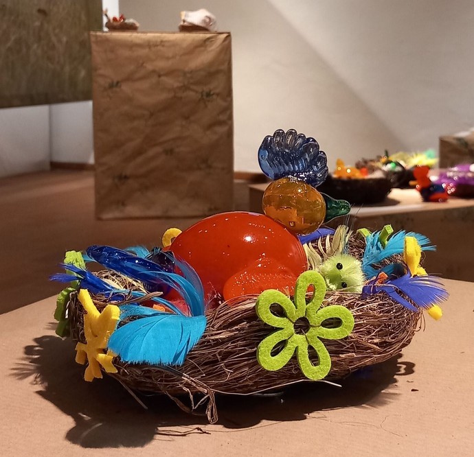 Nest mit einem farbigen Glasvogel und Dekorationen in der Ausstellung.