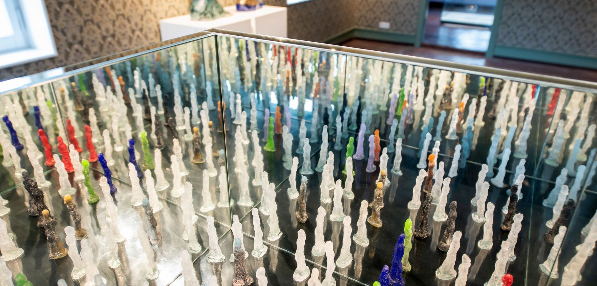 Installation mit vielen kleinen Glasskulpturen in einer verspiegelten Tischvitrine. Arbeit von Korbinian Stöckle mit dem Titel "Zwischenwelt".