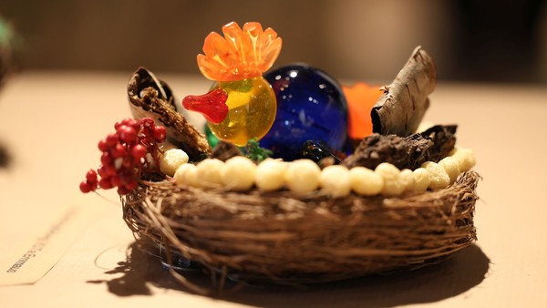 Ein bunter Glasvogel sitzt in einem von einem Kind gebastelten Nest
