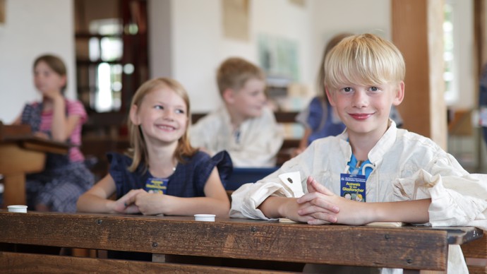 Kinder sitzen hinter historischen Schulbänken. Kinder sitzen hinter historischen Schulbänken.