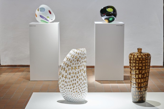 Vier Glasvasen stehen auf Stelen in einer Ausstellung.