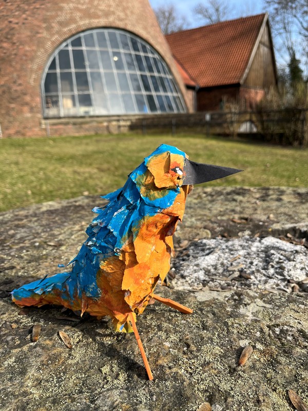 Ein Vogel aus buntem Papier vor dem Glasturm der Glashütte Gernheim