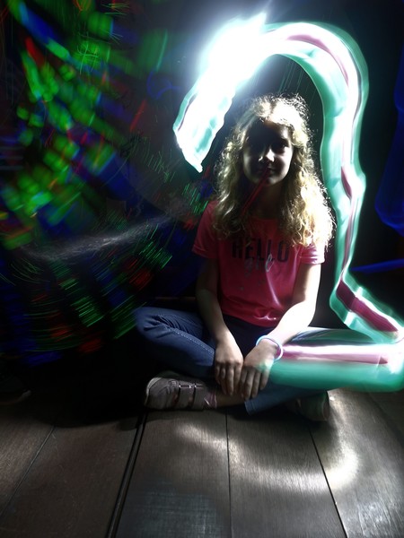 Foto eines sitzenden Mädchens mit hellen Lichtschweifen erstellt mit der Technik Lightpainting.